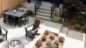 A modern house with a dark exterior, a covered patio with outdoor furniture, and a well-maintained garden.