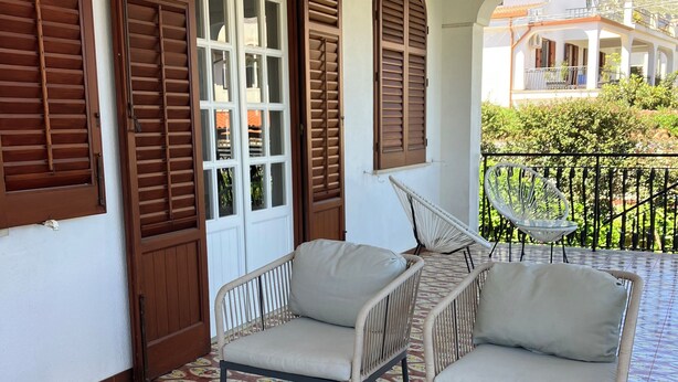 A balcony with two wicker chairs, a table with a decorative plate, and patterned floor tiles.