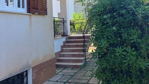 A residential building with a staircase leading to a balcony, surrounded by greenery.