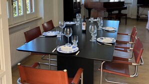 A dining area with a long table set for six, surrounded by red chairs, a piano, and a television.