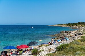 A rocky beach with clear blue water, umbrellas, and people relaxing.