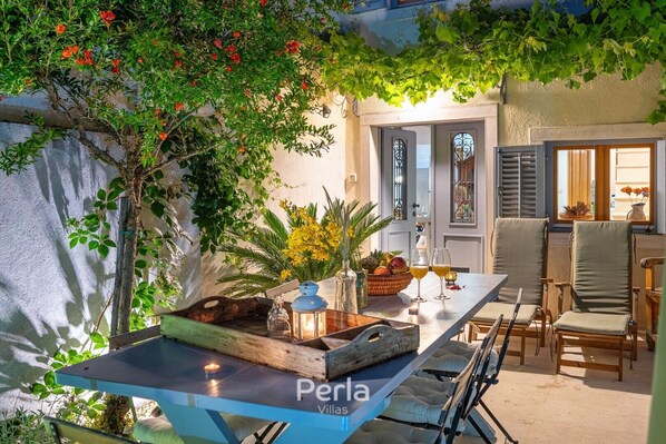 An outdoor patio with a table set for two, surrounded by chairs, and a wooden bench.