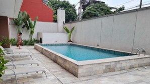 Une piscine rectangulaire bordée de pierres, entourée d’une terrasse carrelée avec des chaises en métal.