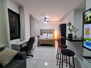 Ein Hotelzimmer mit Bett, Schreibtisch, Stuhl, Fernseher und einem kleinen Tisch mit Pflanze.