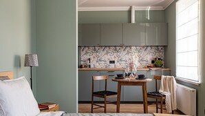 Un dormitorio con cama, mesita de noche, lámpara y vistas a una cocina con ventana.