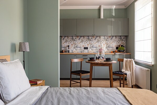 Un dormitorio con cama, mesita de noche, lámpara y vistas a una cocina con ventana.