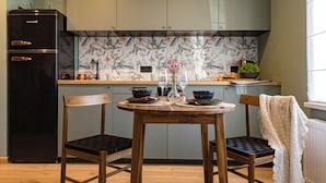Una cocina con un refrigerador negro, sillas de madera, una mesa redonda y un salpicadero con diseño floral.