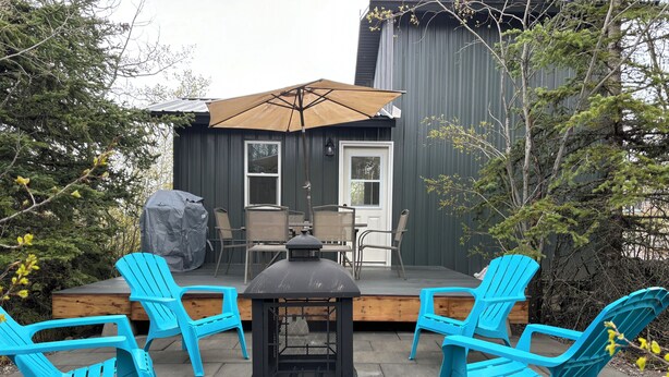 En terrass med fyra blå stolar, ett bord och ett stort parasoll.