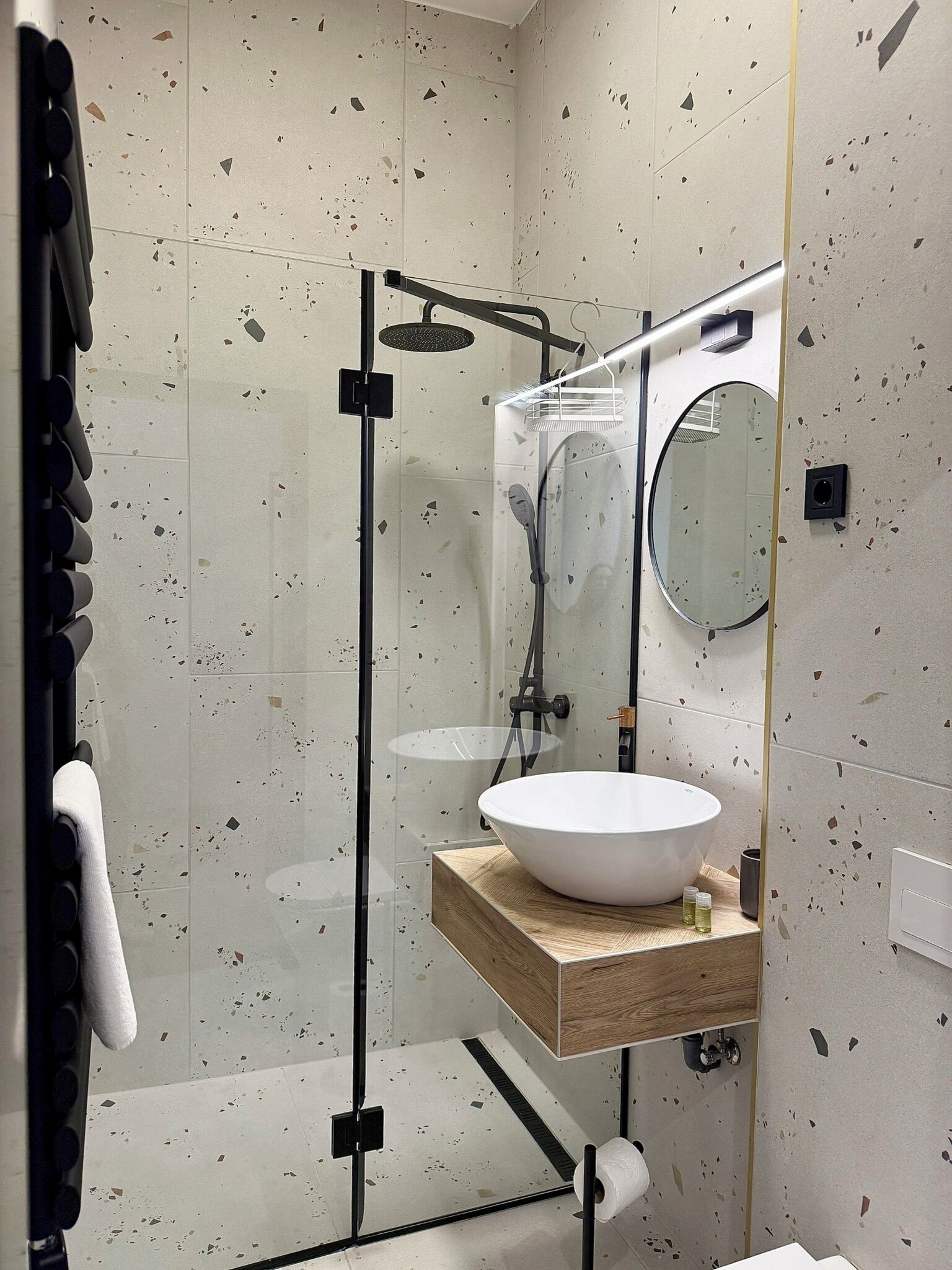 A modern bathroom with a glass-enclosed shower, a round mirror, and a wooden vanity.