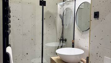 A modern bathroom with a glass-enclosed shower, a round mirror, and a wooden vanity.