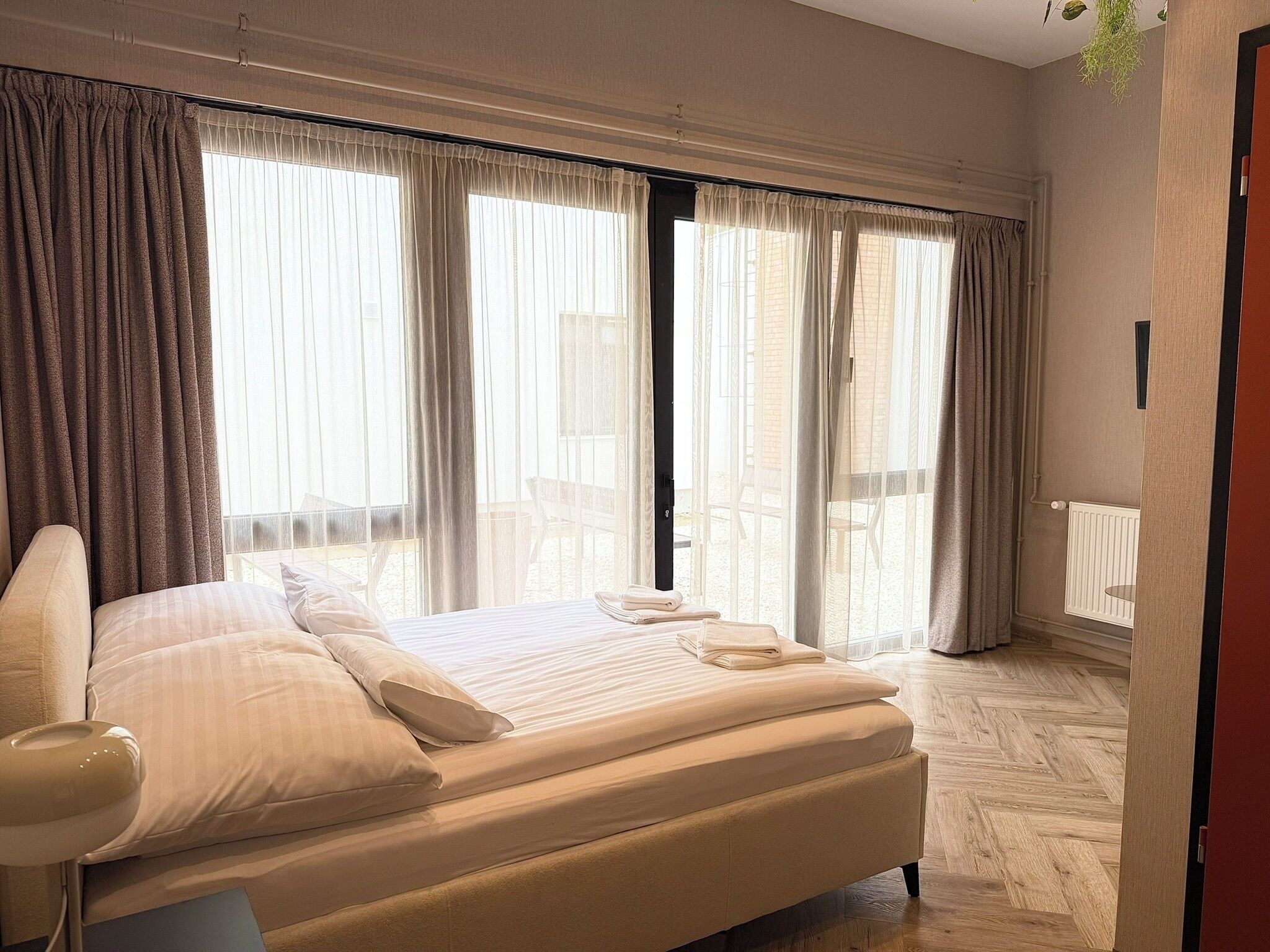 A hotel room with a bed, curtains, a window, and a radiator.