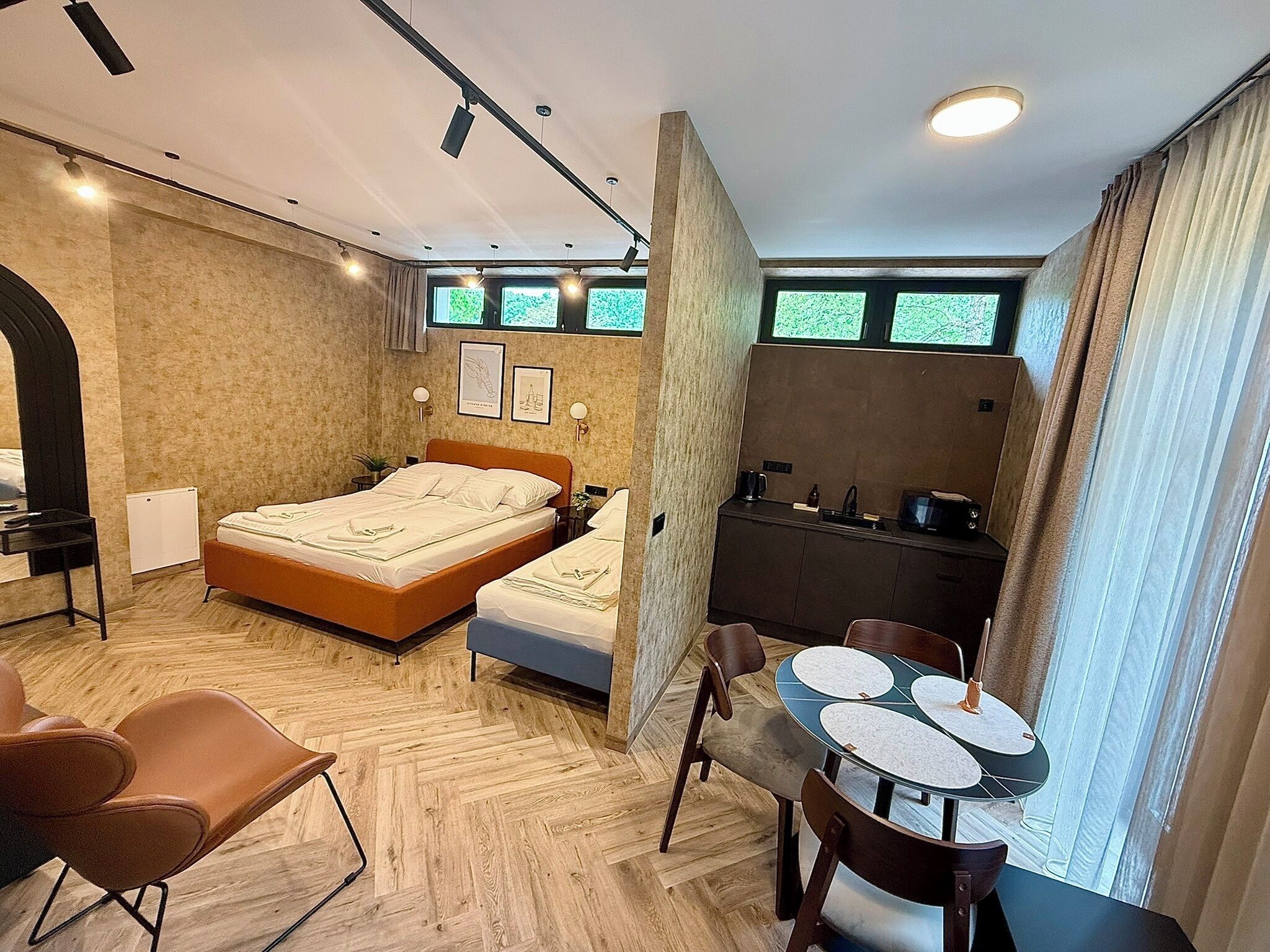 Una habitación de hotel moderna con cama, una pequeña kitchenette, un área de comedor y un amplio ventanal.