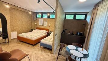 Una habitación de hotel moderna con cama, una pequeña kitchenette, un área de comedor y un amplio ventanal.