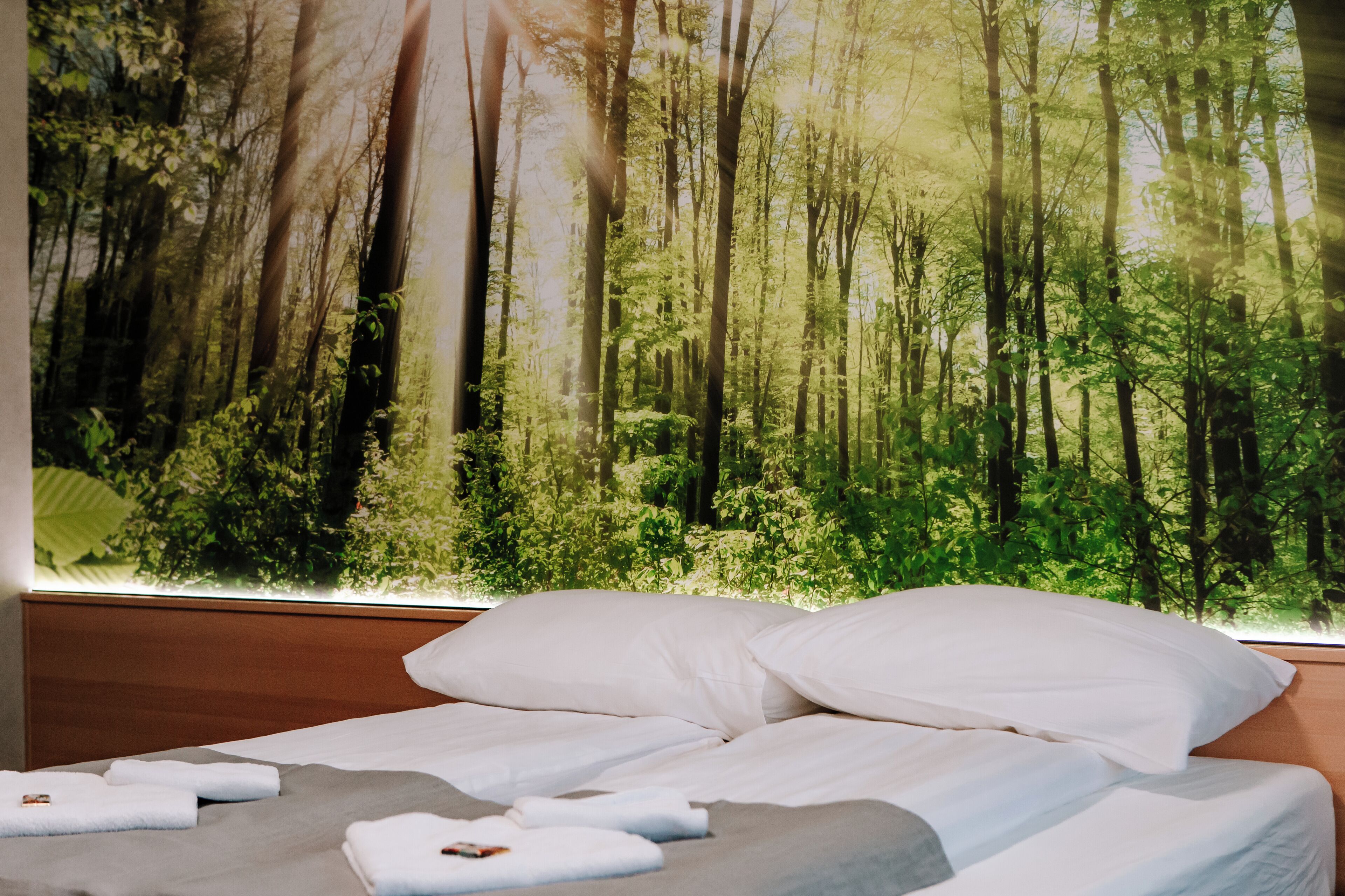 A bedroom with a bed, pillows, and a large forest mural on the wall.