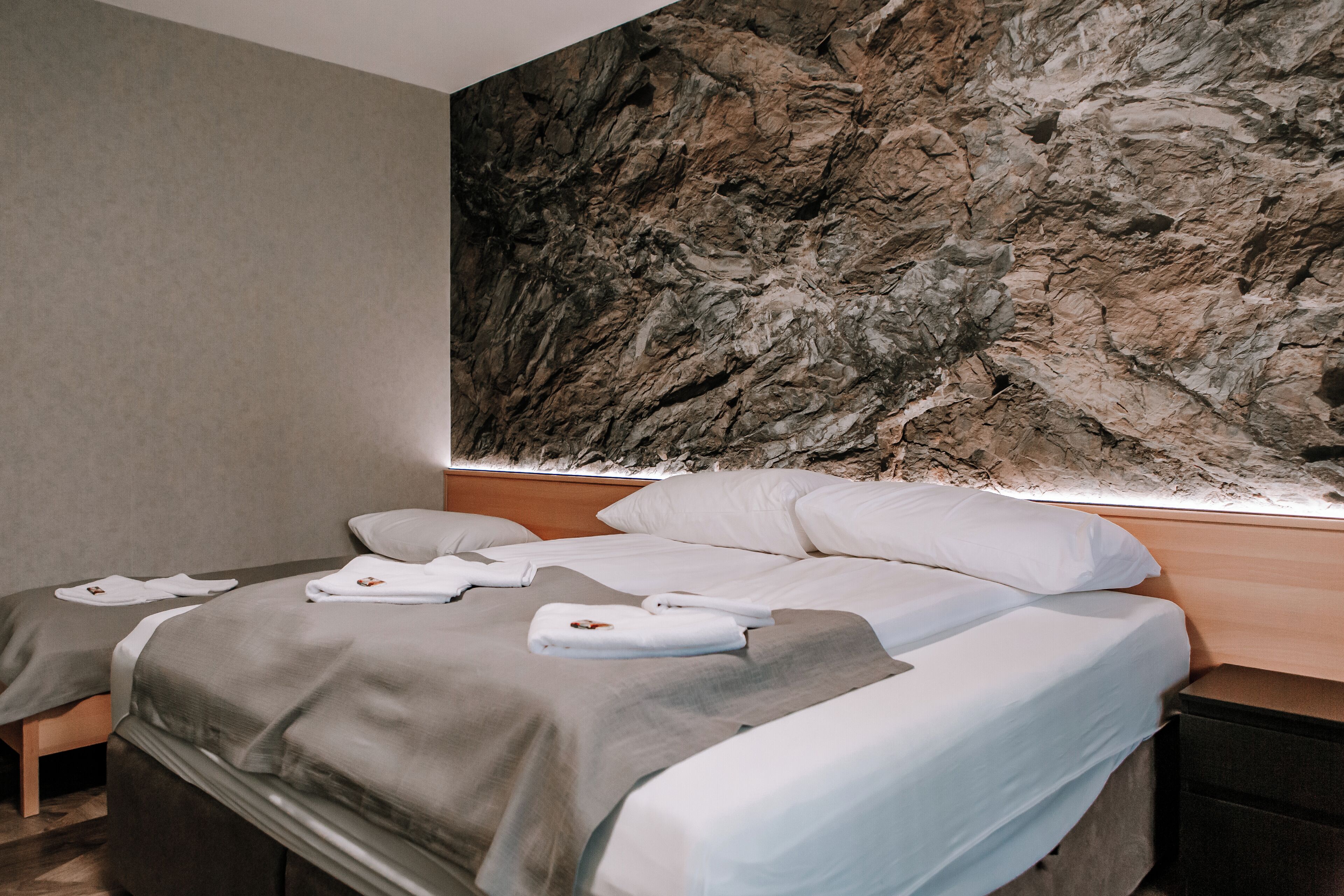 Una habitación de hotel con una cama, una mesita de noche y un mural grande de una pared de roca.