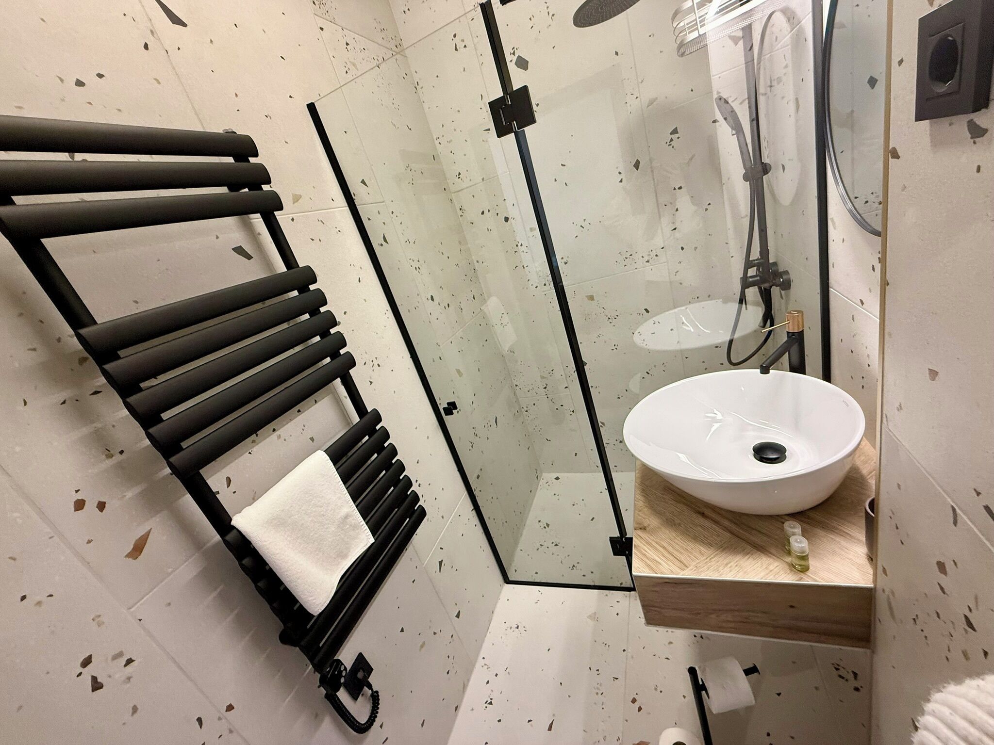 A bathroom with a glass shower enclosure, a white sink, and a towel rack.