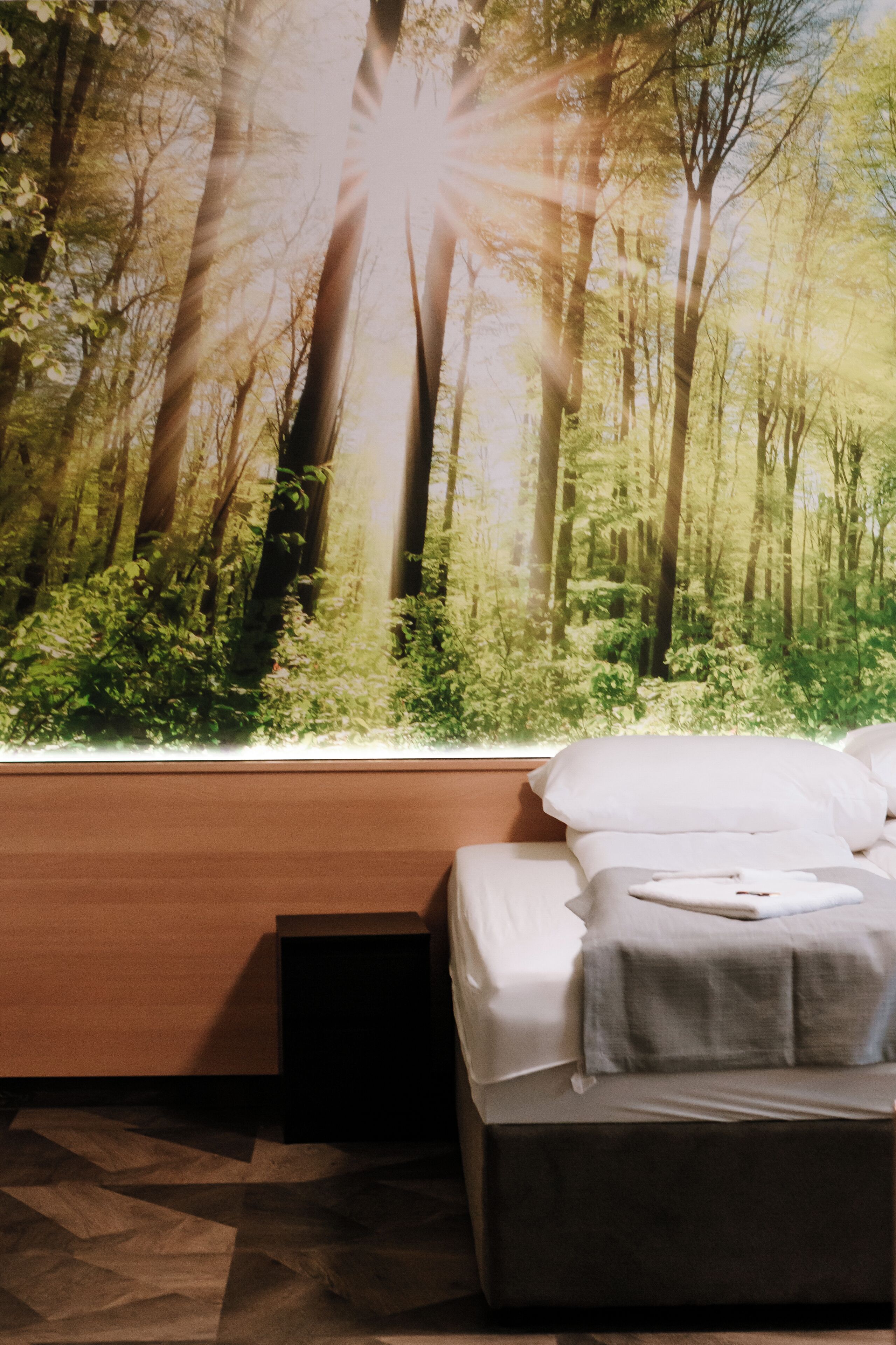 A bedroom with a large forest mural on the wall, a bed with white bedding, and a wooden headboard.