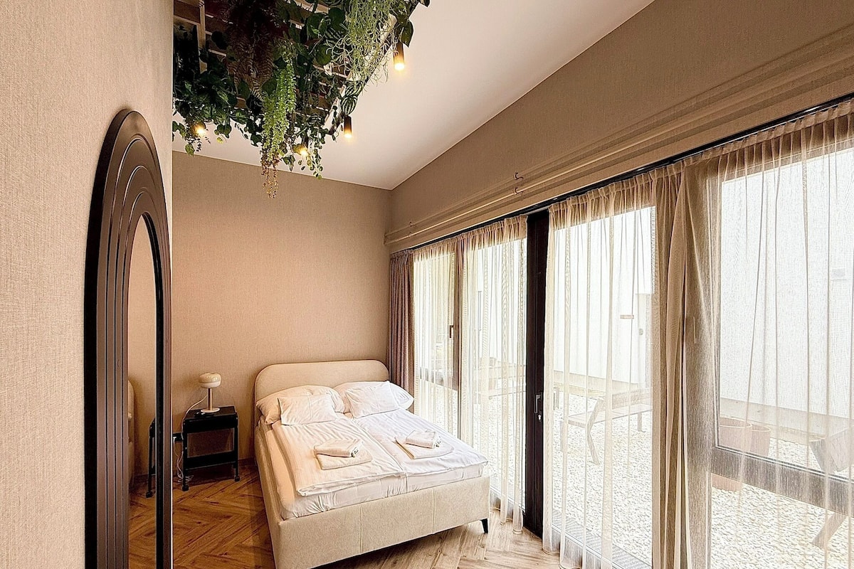 Une chambre à coucher avec un lit, un miroir, une table de chevet et une plante suspendue.