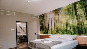 Un dormitorio con un gran mural de un bosque, una cama con ropa de cama blanca y un baño con accesorios modernos.