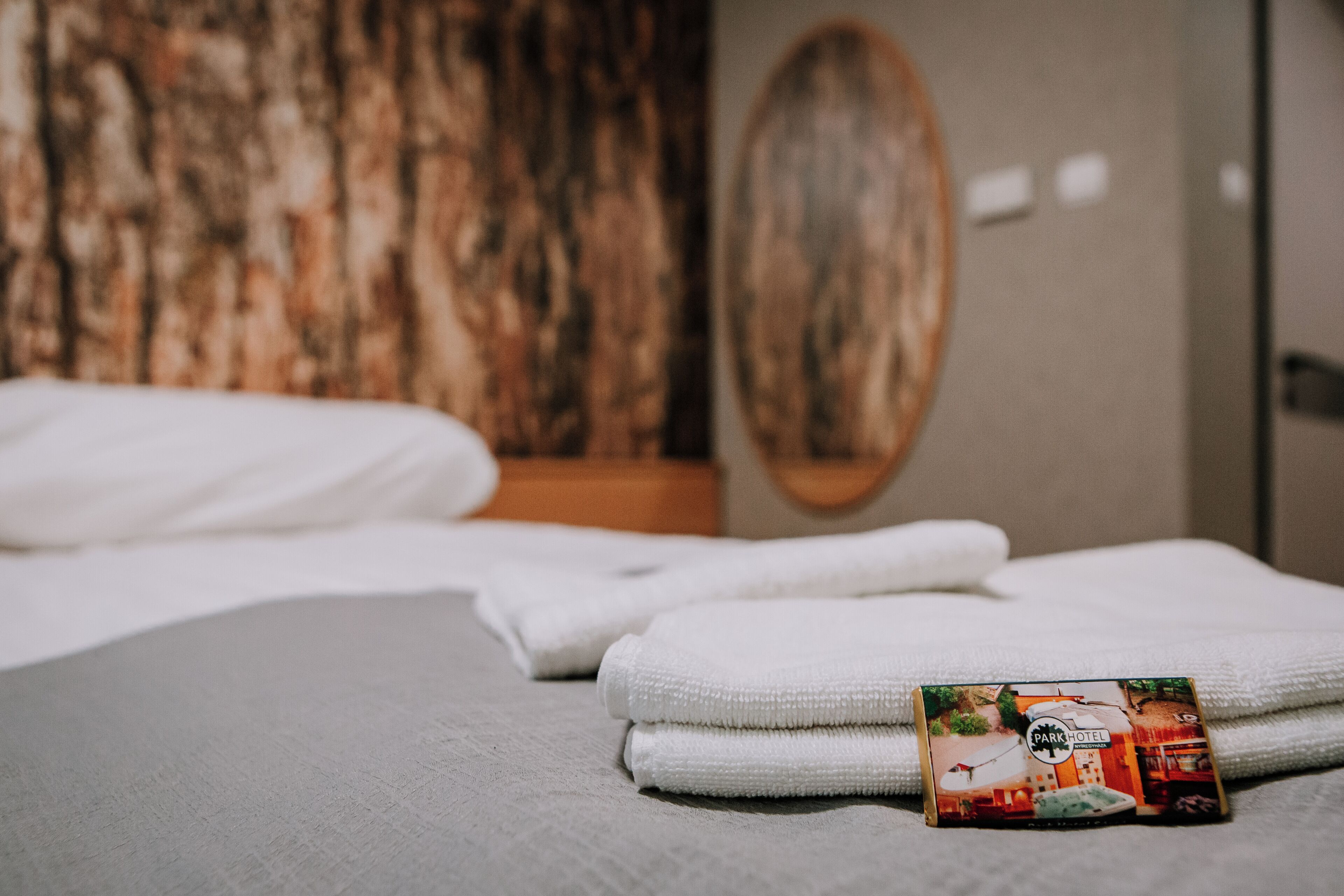 A neatly made bed with white linens and a folded towel on a textured gray surface.