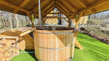 A wooden hot tub under a covered area with a view of a house in the background.