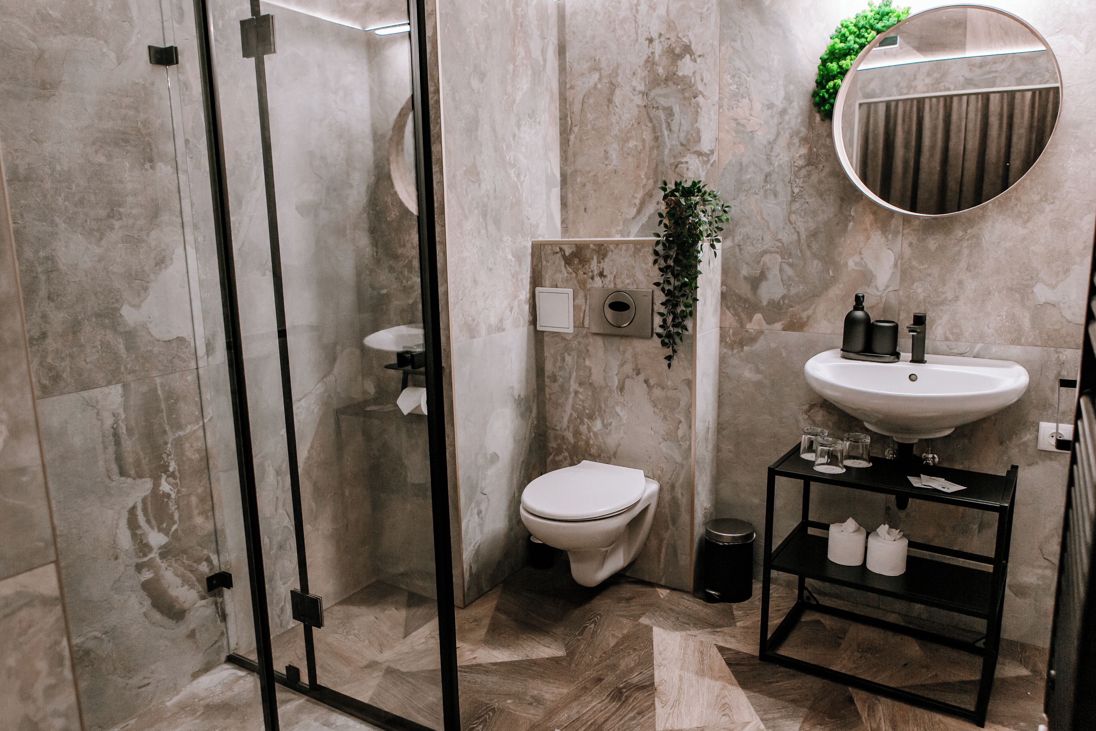 A modern bathroom with a glass shower enclosure, a toilet, a sink with a mirror, and a small shelf with toiletries.