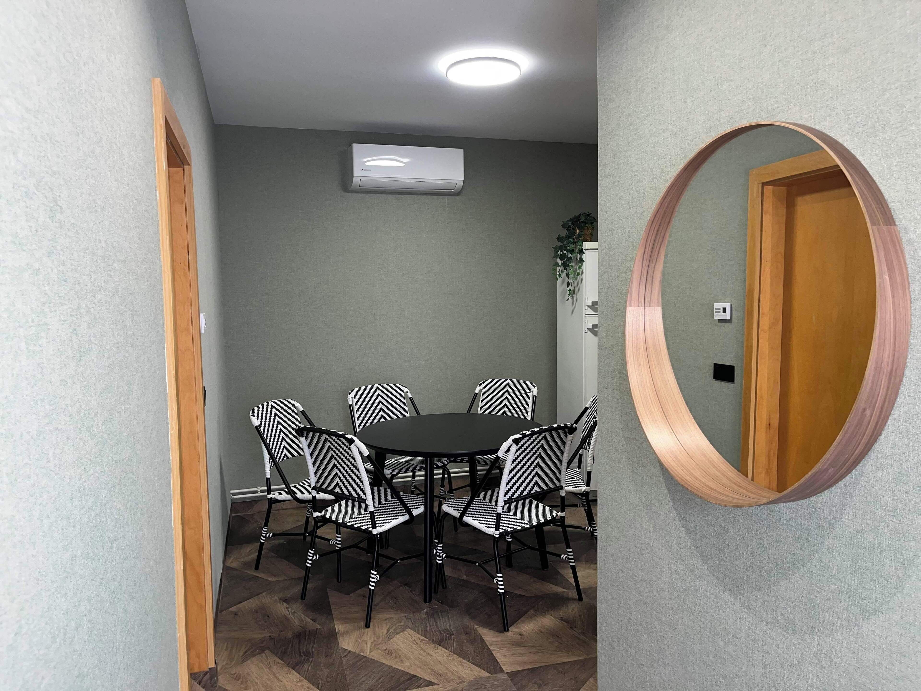 Un salón de conferencias con una mesa redonda, seis sillas y un equipo de aire acondicionado en la pared.