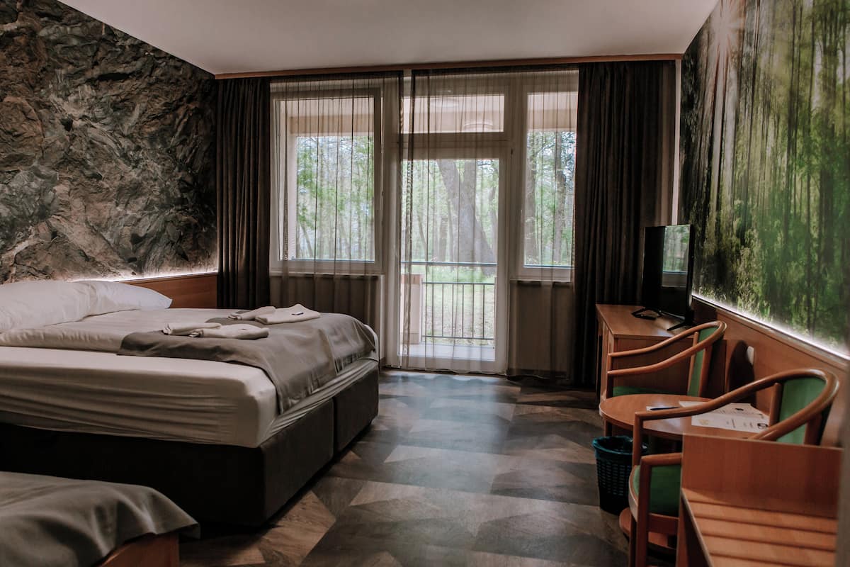 Une chambre d’hôtel comprenant un lit, un bureau avec des chaises, une télévision et une grande fenêtre avec des rideaux.