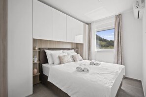 A modern bedroom with a large bed, built-in shelving, and a window with a view of greenery.
