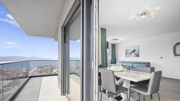 Un balcon avec vue sur les immeubles, un coin repas avec une table et des chaises, et un luminaire au plafond.