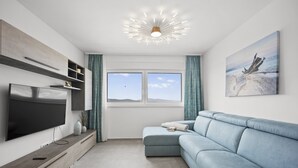 Un salon moderne dot é d’un téléviseur à écran plat, d’un canapé bleu clair et d’une grande fenêtre offrant une vue sur le ciel.
