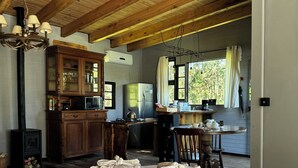 Ein gemütliches Blockhäuschen im Inneren mit Holzbalkendecke, einem Essbereich mit Tisch und Stühlen, einer Küchenzeile mit Kühlschrank und einem großen Fenster, das für natürliches Licht sorgt.