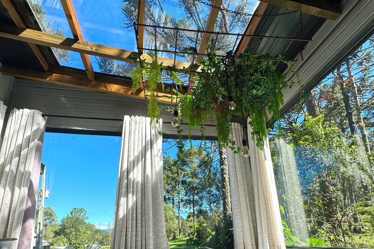 A wooden deck with a hot tub, white curtains, and a view of trees and a lawn.