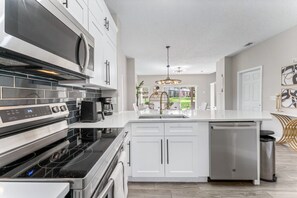 A modern kitchen with white cabinetry, a black stovetop, and a built-in dishwasher. - 8496 Resort 3BR Condo by Disney World Orlando (Kissimmee)