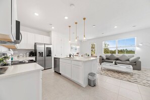 A modern kitchen with white cabinetry, stainless steel appliances, and pendant lighting.