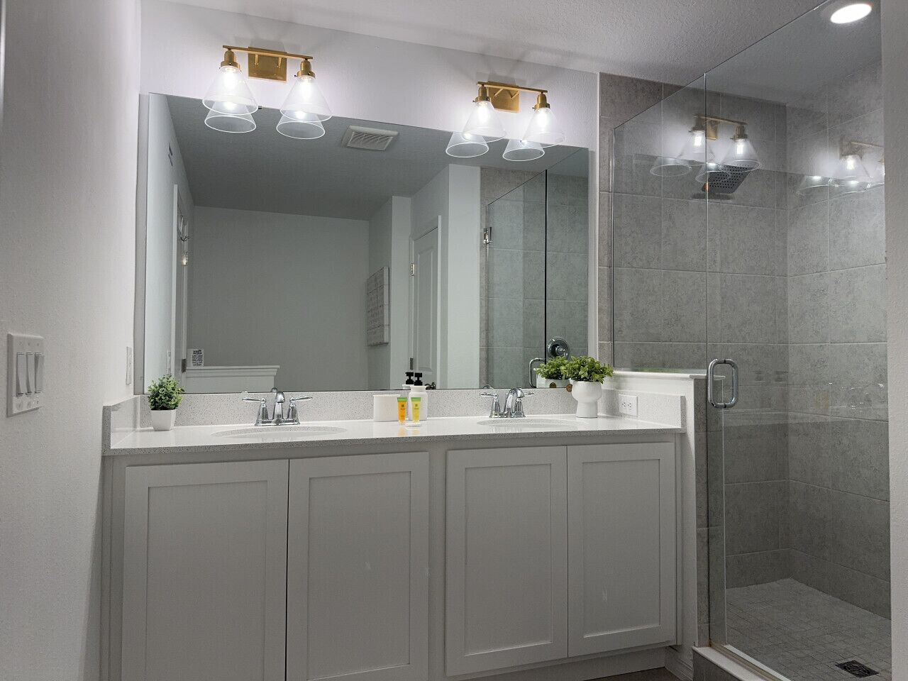 A bathroom with a double sink vanity, a large mirror, and a glass shower enclosure.