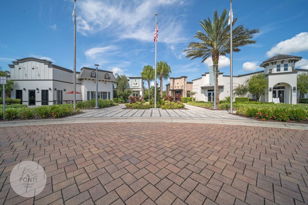 A paved walkway leading to a building with a flagpole, palm trees, and a clear blue sky.