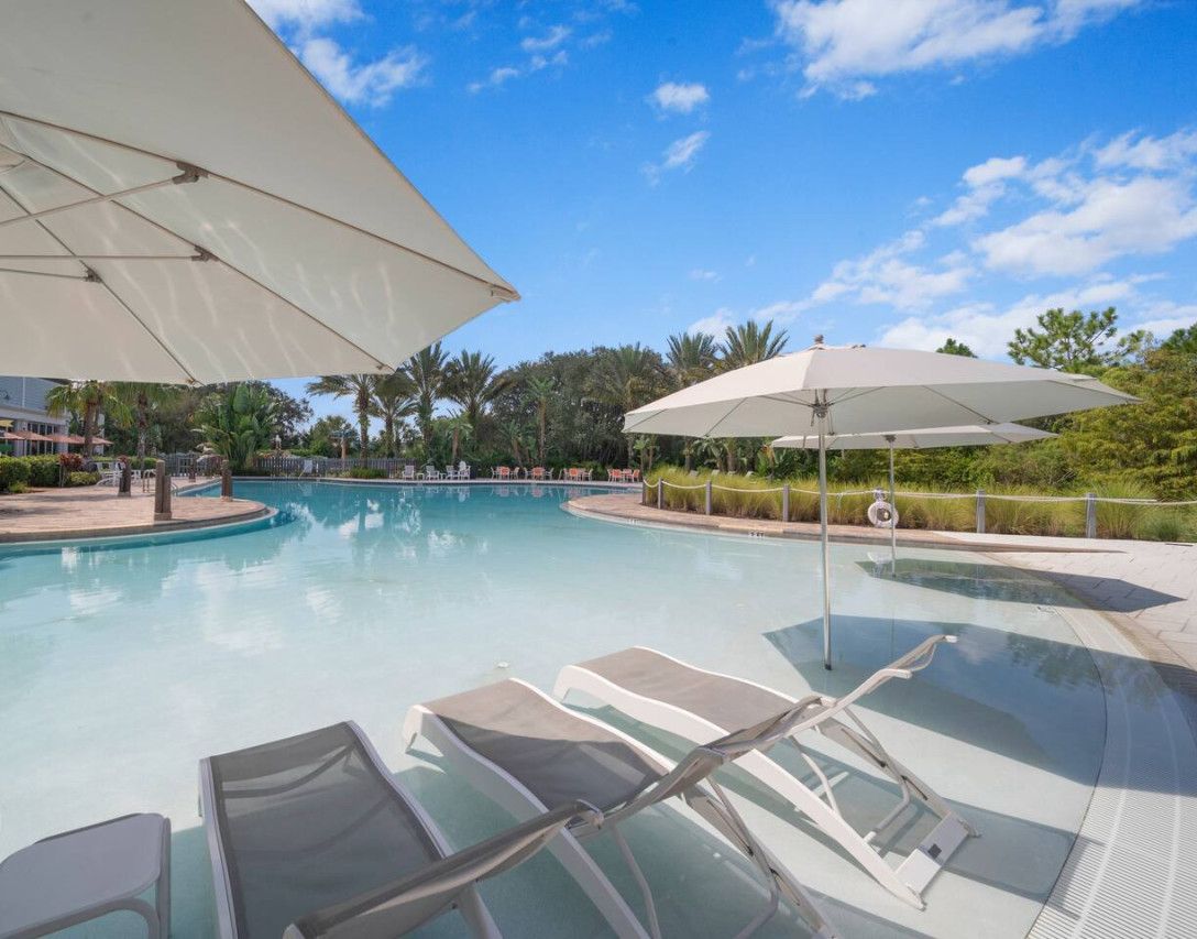 A swimming pool with lounge chairs and umbrellas, surrounded by greenery and a clear sky.