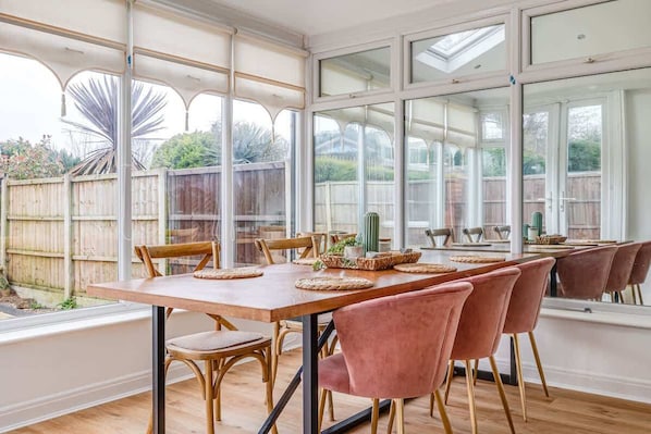 Un espace repas avec une longue table, des chaises et une vue dégagée grâce à de grandes fenêtres.