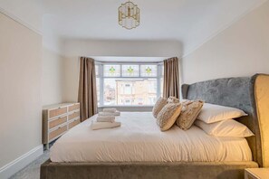 A bedroom with a large bed, a nightstand, a dresser, and a window with curtains.