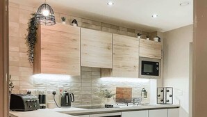 A modern kitchen with a central island, wooden cabinets, a microwave, and bar stools. - Stylish 1Bed Apartment in Sheffield CC (Sheffield)