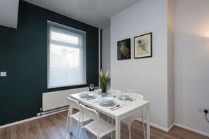A dining area with a white table set for four, a window with blinds, and two framed pictures on the wall. - Stylish 3BR House in Hull - Sleeps 5 (Hull)