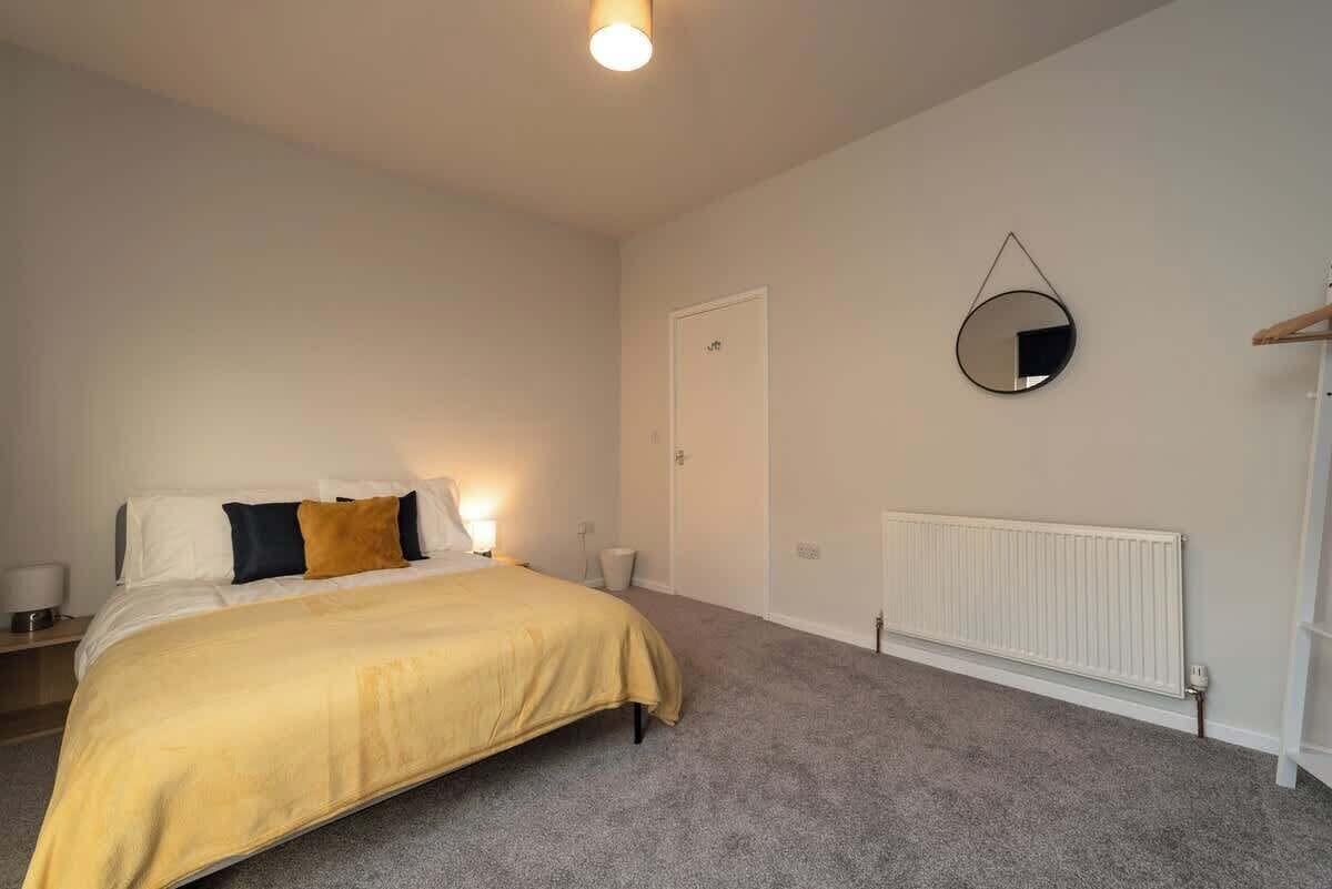 A bedroom with a bed, bedside lamps, a mirror, a radiator, and a door.