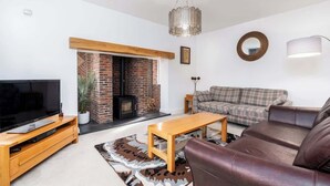A living room with a TV, sofa, coffee table, fireplace, and a hanging light fixture. - Beautiful Big Family Home: Sleeps 10, Park 3 Cars! (Leeds)