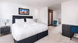 A modern bedroom with a large bed, bedside tables, a desk, and a chair. - Beautiful Big Family Home: Sleeps 10, Park 3 Cars! (Leeds)