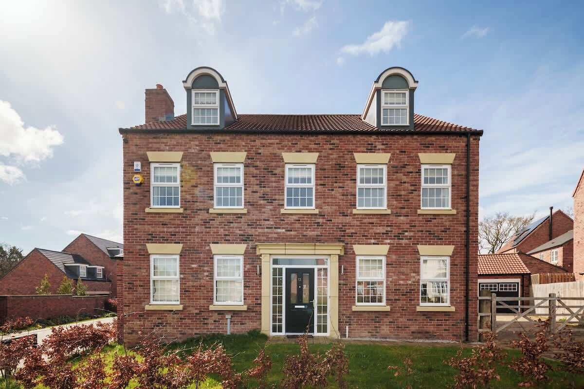 Une maison à deux étages, construite en briques, avec une façade symétrique, une entrée centrale et un petit jardin à l’avant.