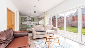 A spacious living area with a sofa, a coffee table, and a view of the backyard through large sliding glass doors. - Beautiful Big Family Home: Sleeps 10, Park 3 Cars! (Leeds)