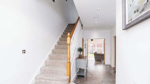 A staircase with a wooden handrail, a light blue console table, and a door leading to a room with a wicker chair. - Beautiful Big Family Home: Sleeps 10, Park 3 Cars! (Leeds)
