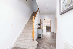 A staircase with a wooden handrail, a light blue console table, and a door leading to a room with a wicker chair. - Beautiful Big Family Home: Sleeps 10, Park 3 Cars! (Leeds)