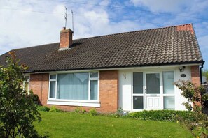 Uma casa de dois andares com telhado telhado, fachada de tijolos e um jardim frontal.
